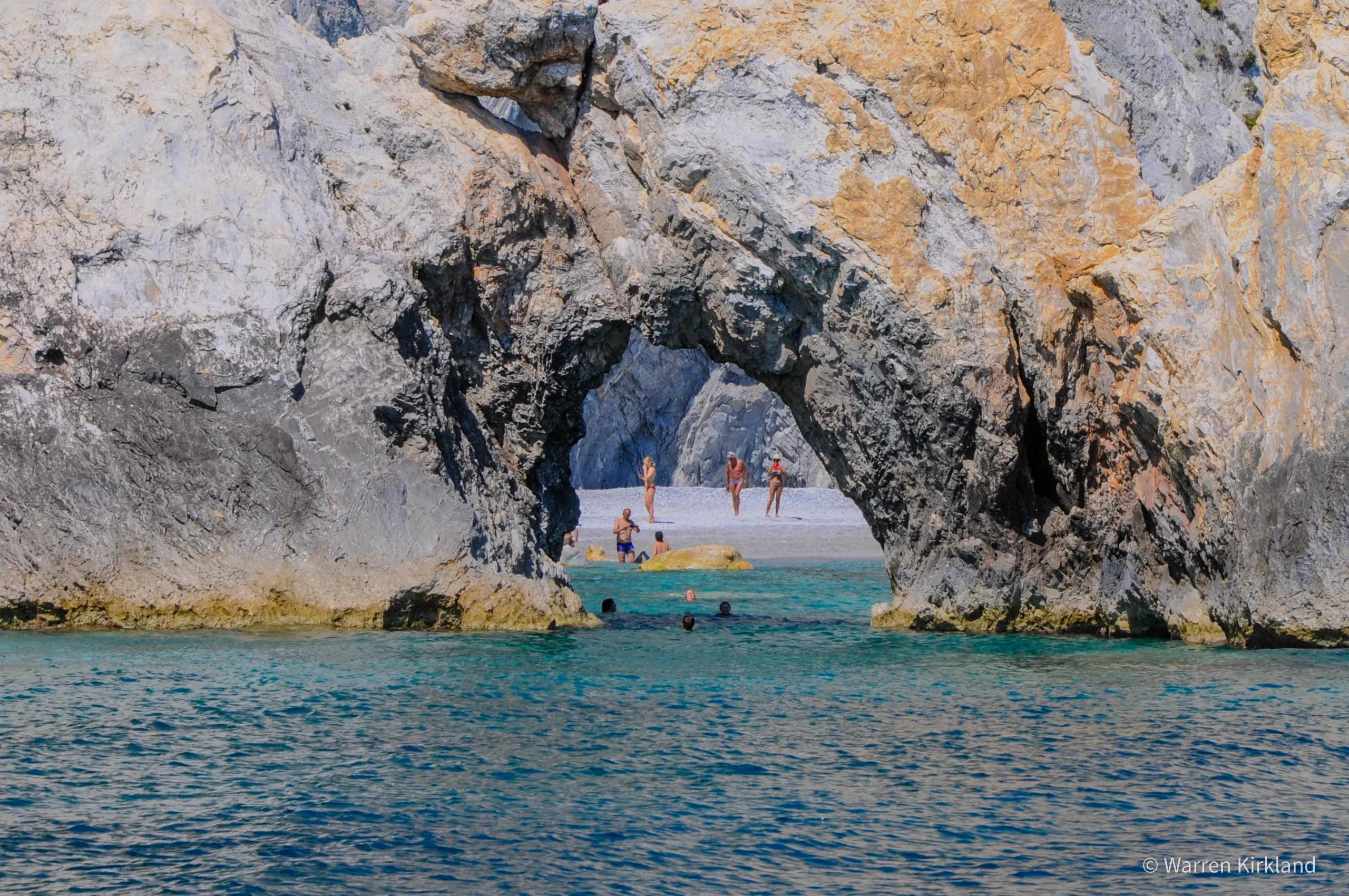 Swimmers in a turquoise cove framed by a rock archway
