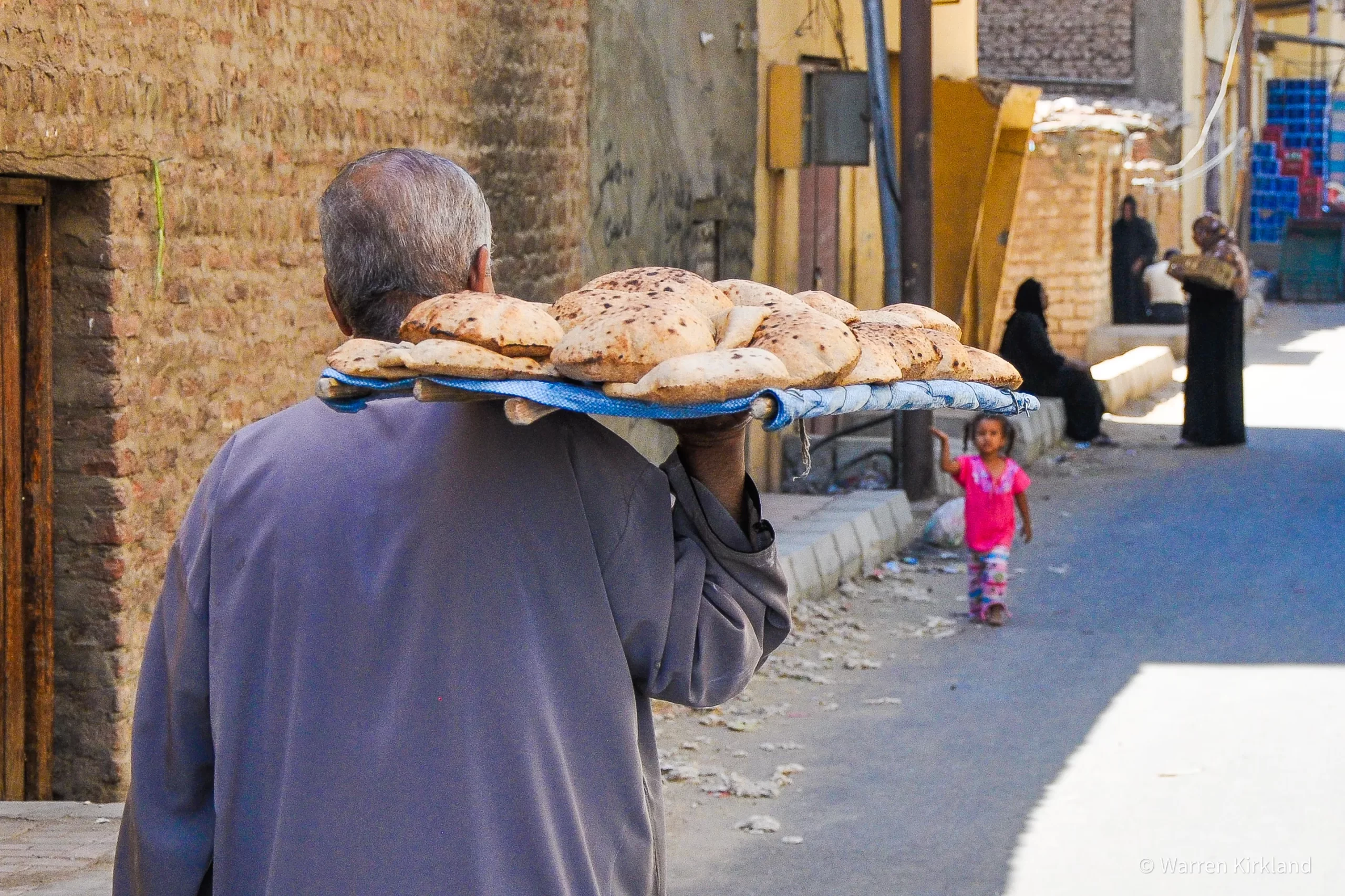 Bread vendor carrying stacked loaves through a market street, Egypt