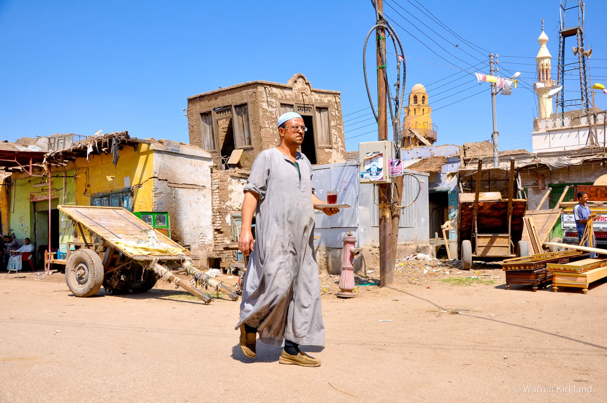 Man standing among old buildings with a mosque minaret in the background, Egypt