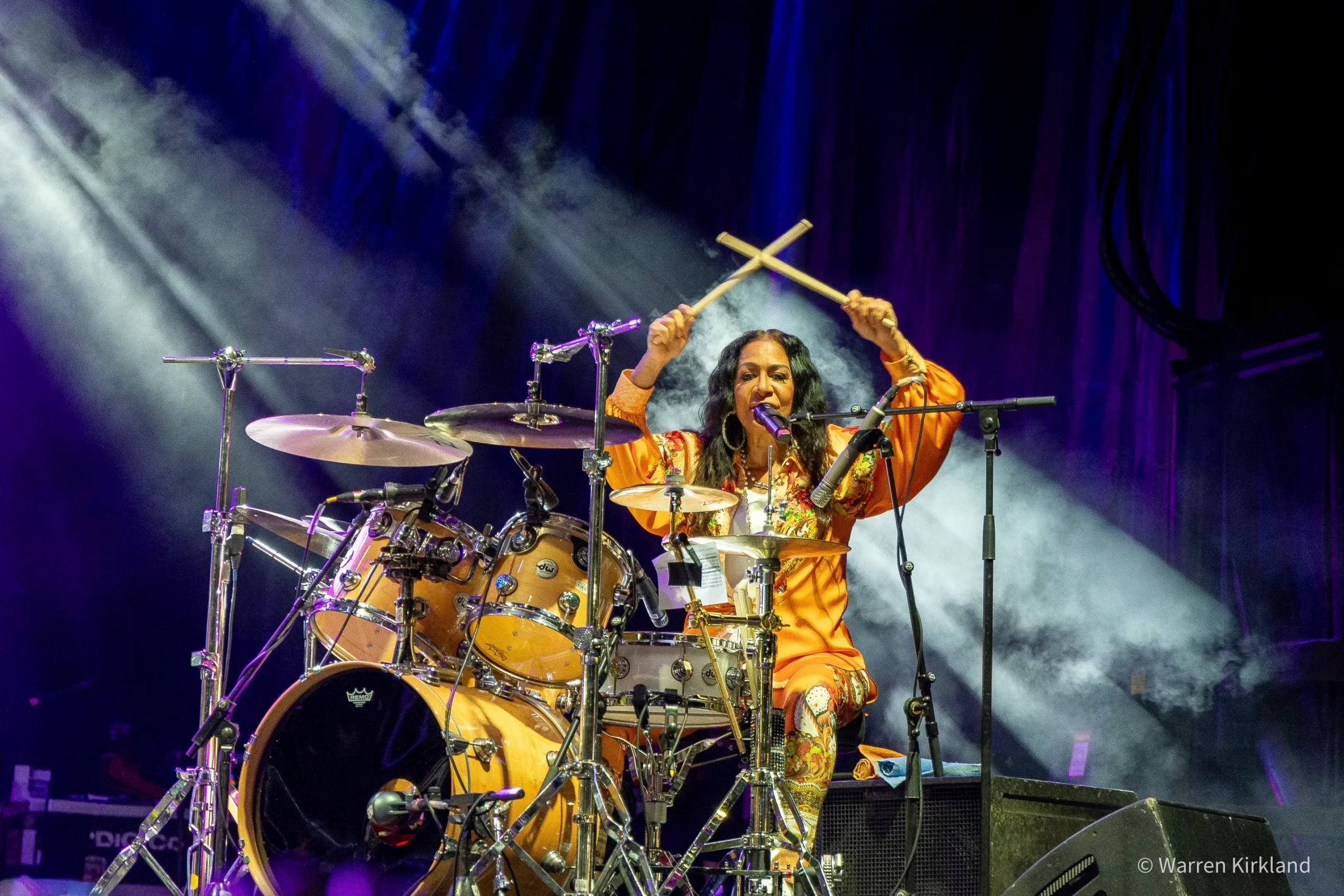 Sheila E. drumming on stage with The E-Train, smoke and stage lights behind