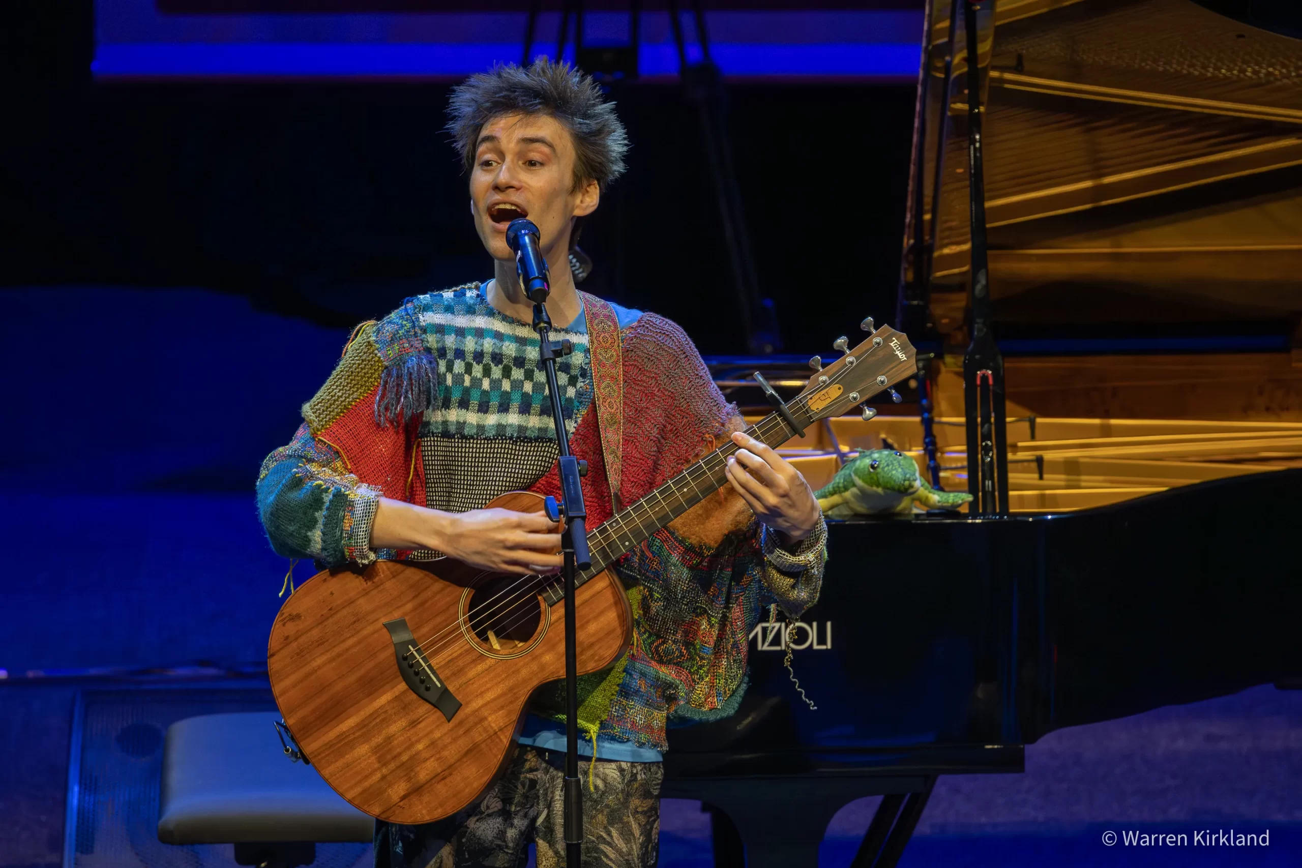 Jacob Collier singing while playing acoustic guitar on stage