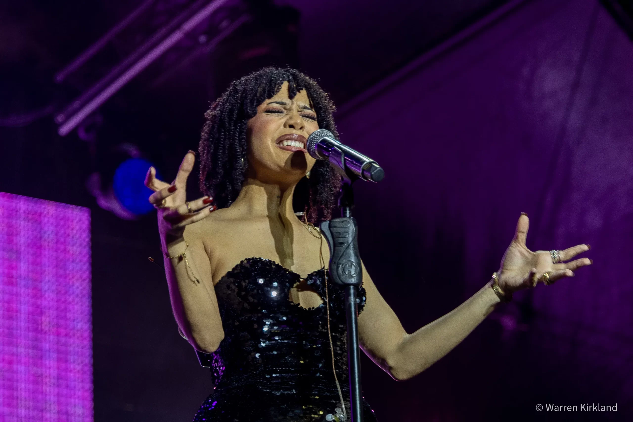 Lordkez singing passionately into a microphone under purple stage lights