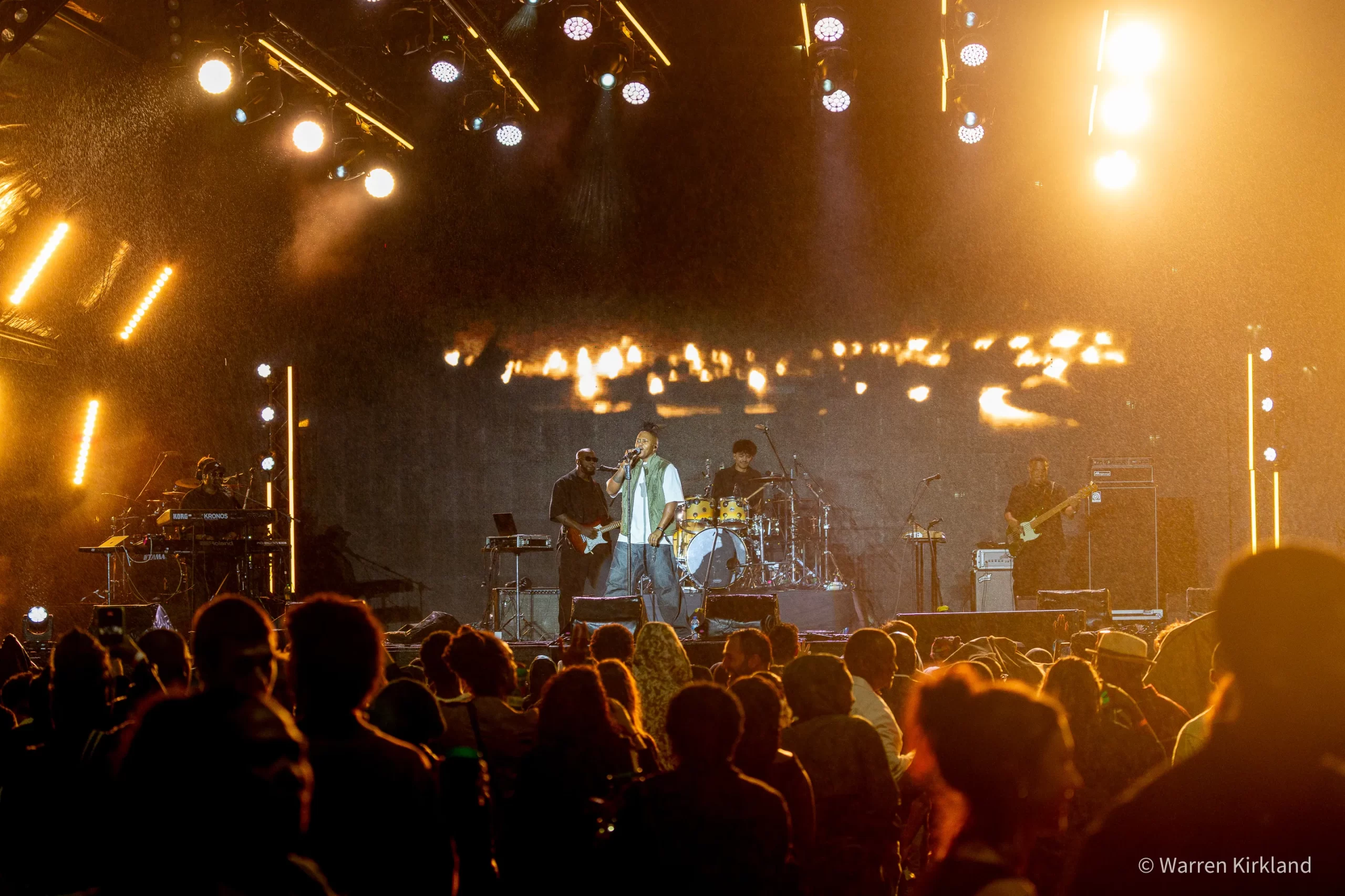 Manana performing with a full band under golden stage lighting