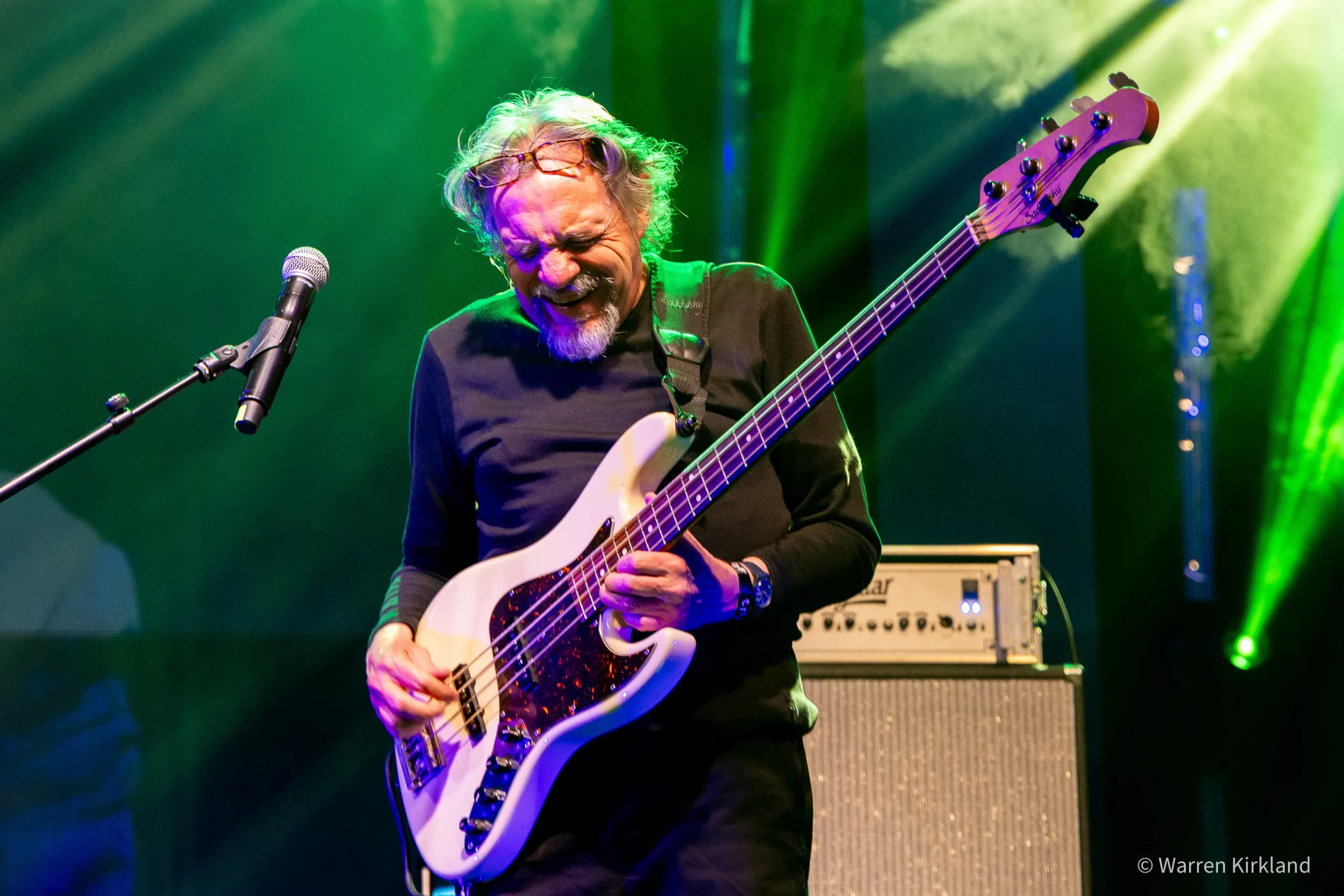 Carlo Mombelli playing bass guitar under green stage lights