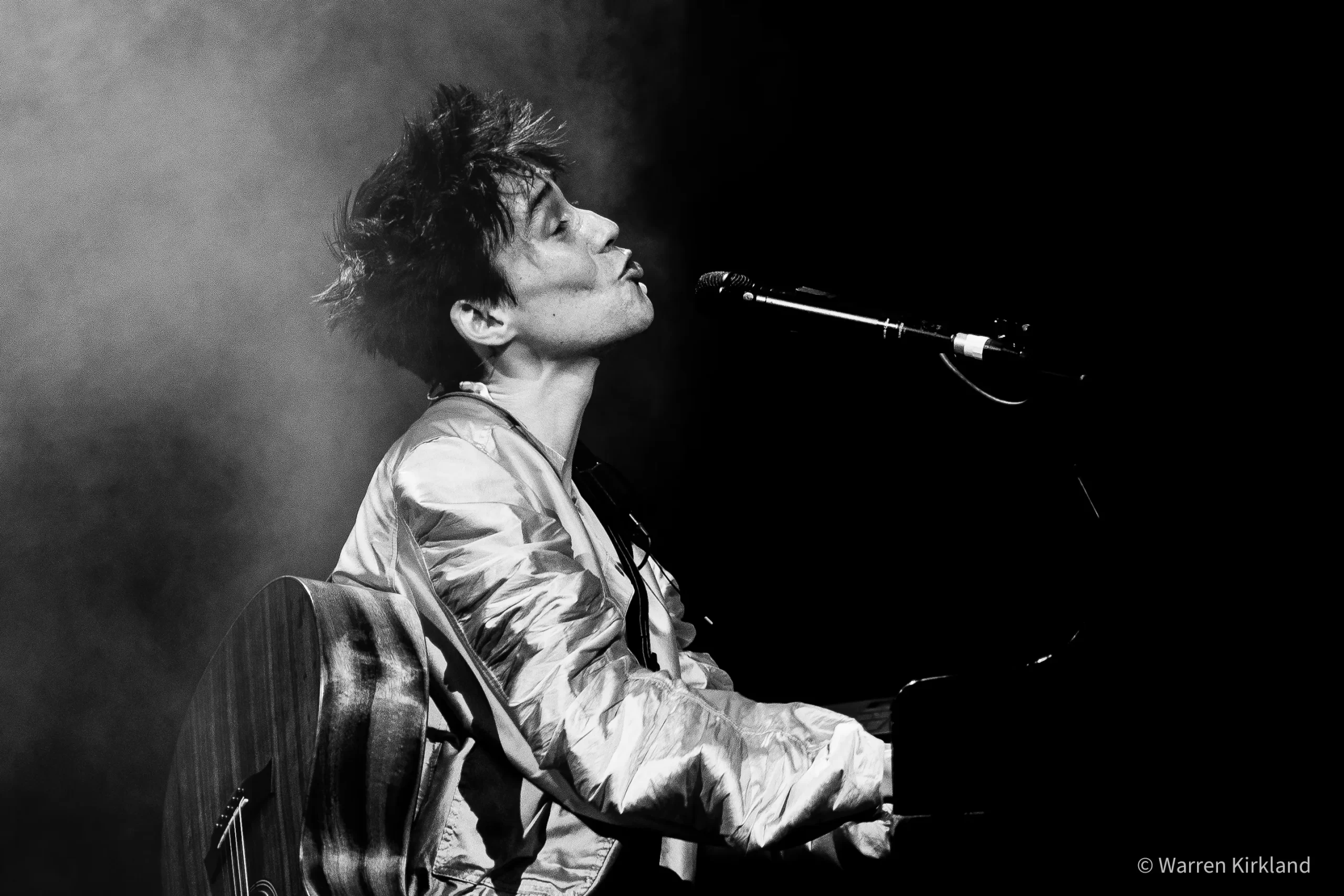 Jacob Collier singing at the microphone while playing piano, black and white
