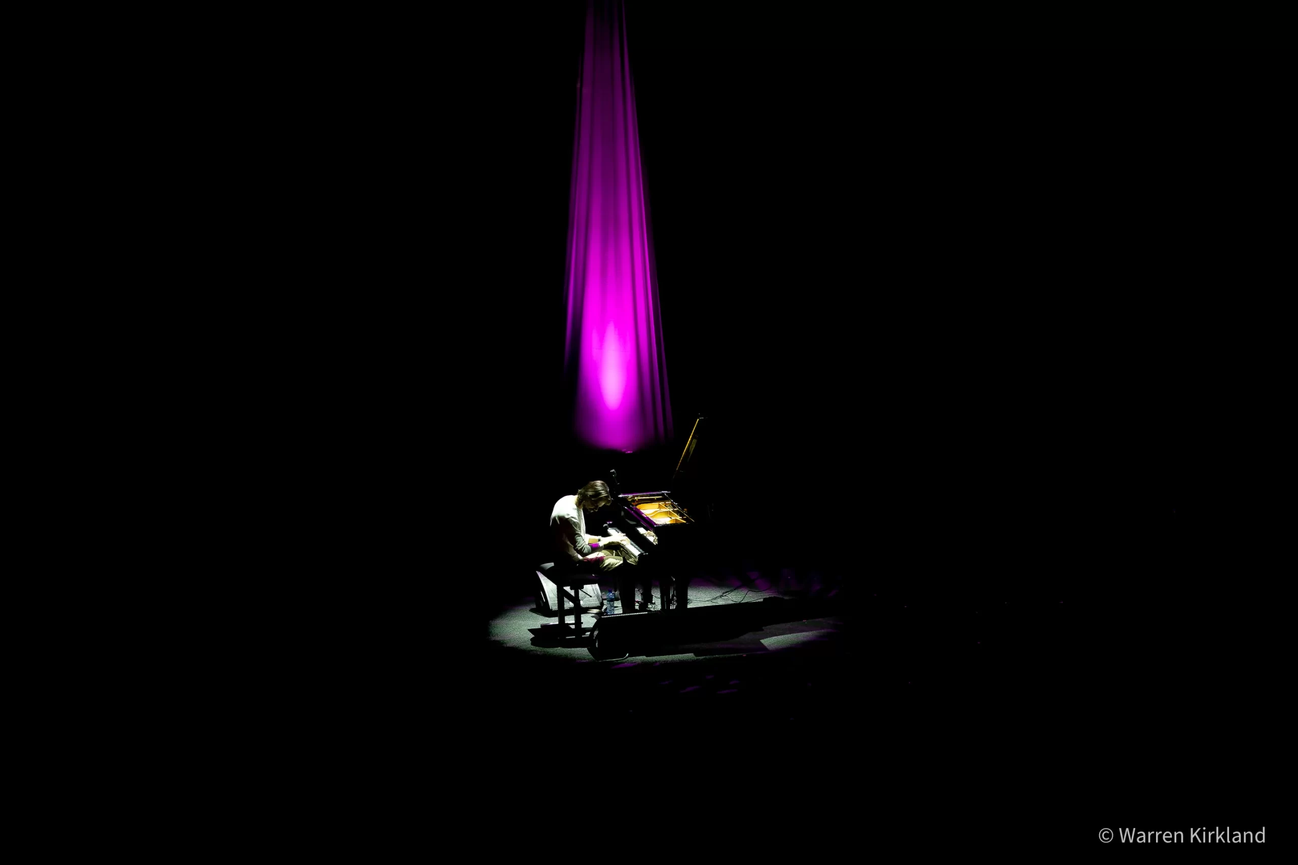Salomão Soares playing piano, spotlit against a dark stage