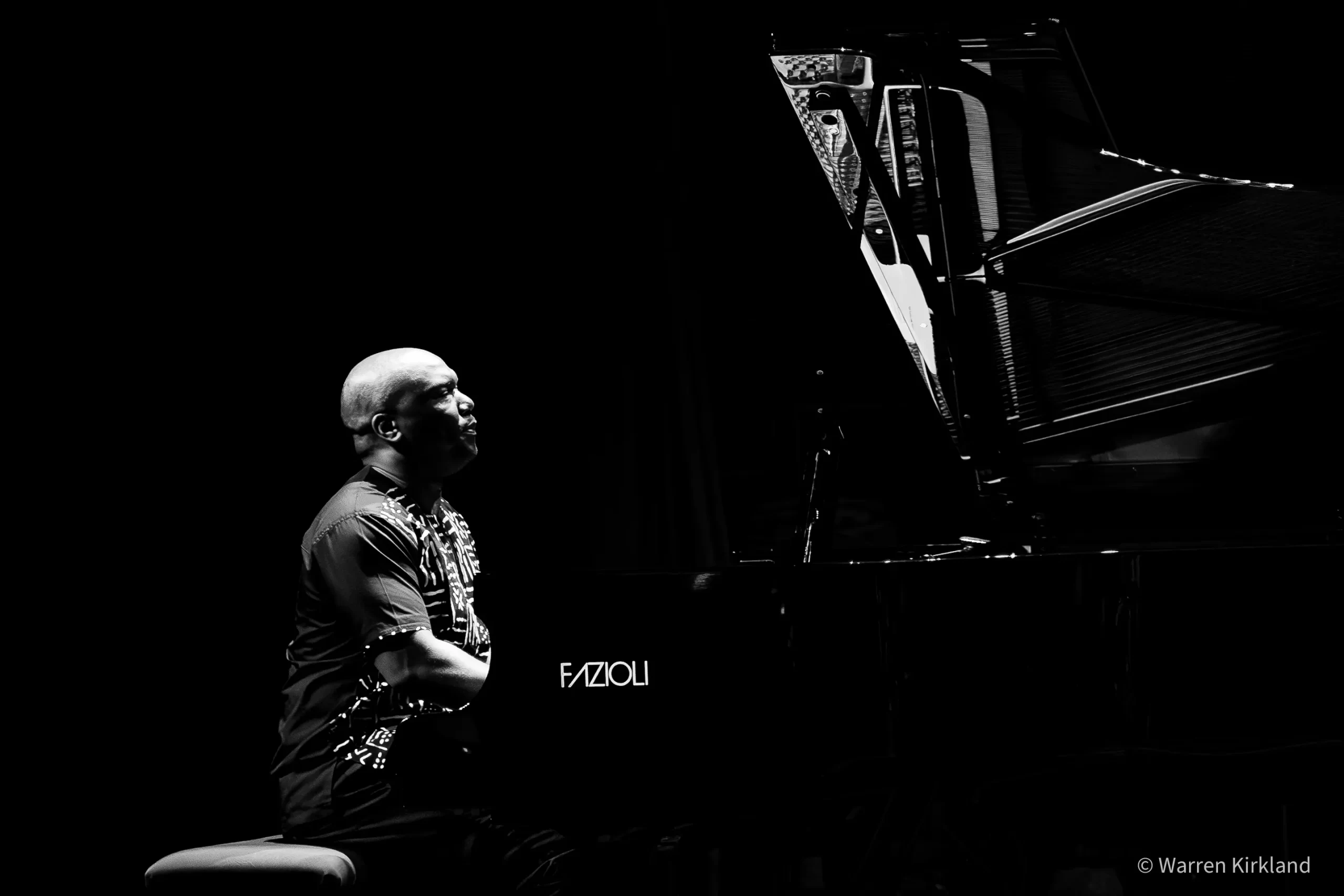 Sibusiso Mash Mashiloane seated beside a grand piano, black and white silhouette