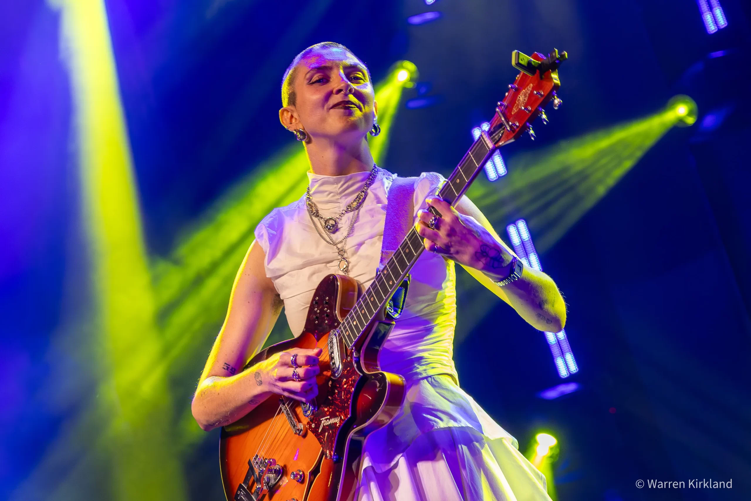 Jasmine Myra playing guitar under crossed green and blue spotlights