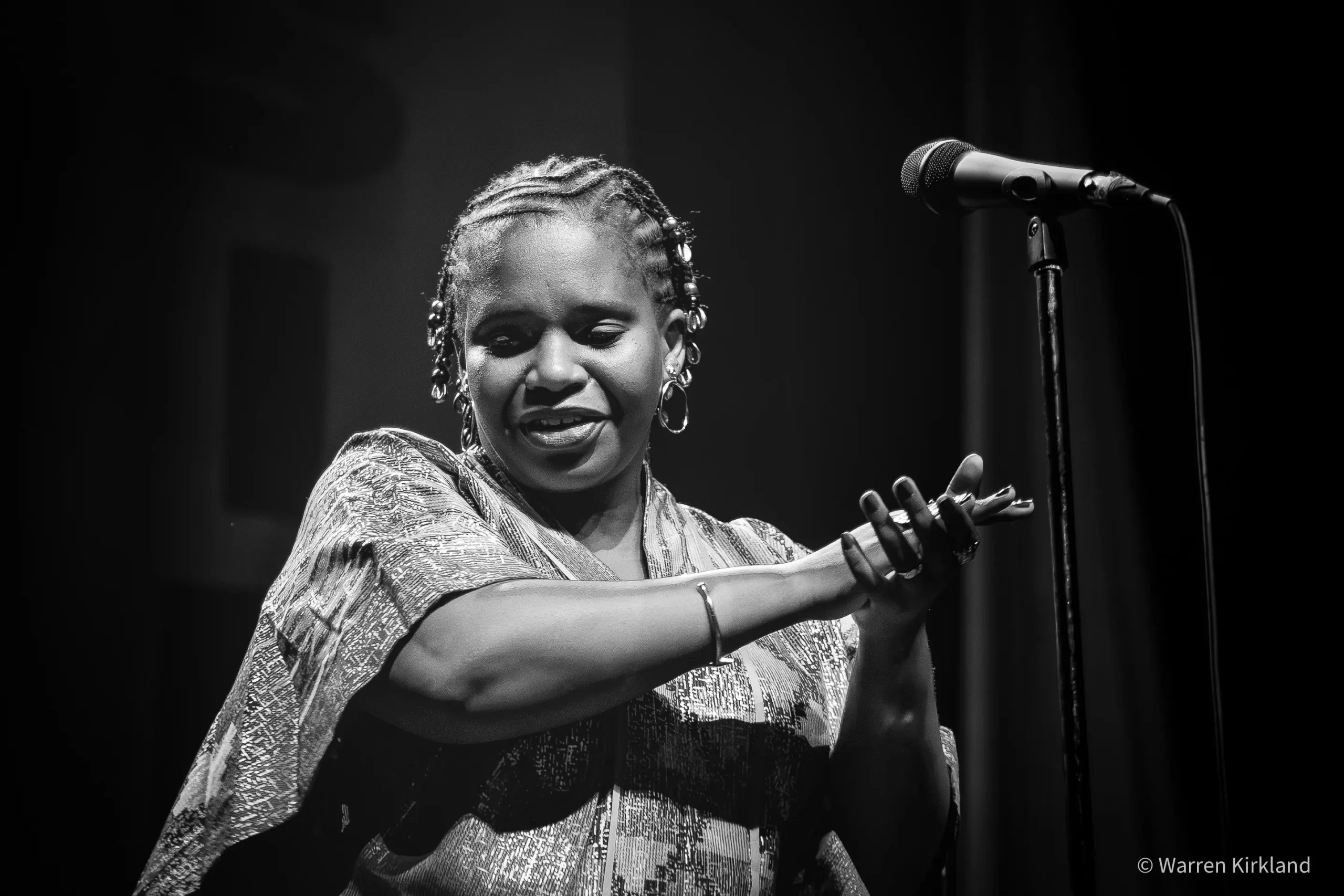 Tutu Puoane singing at the microphone with an expressive hand gesture, black and white