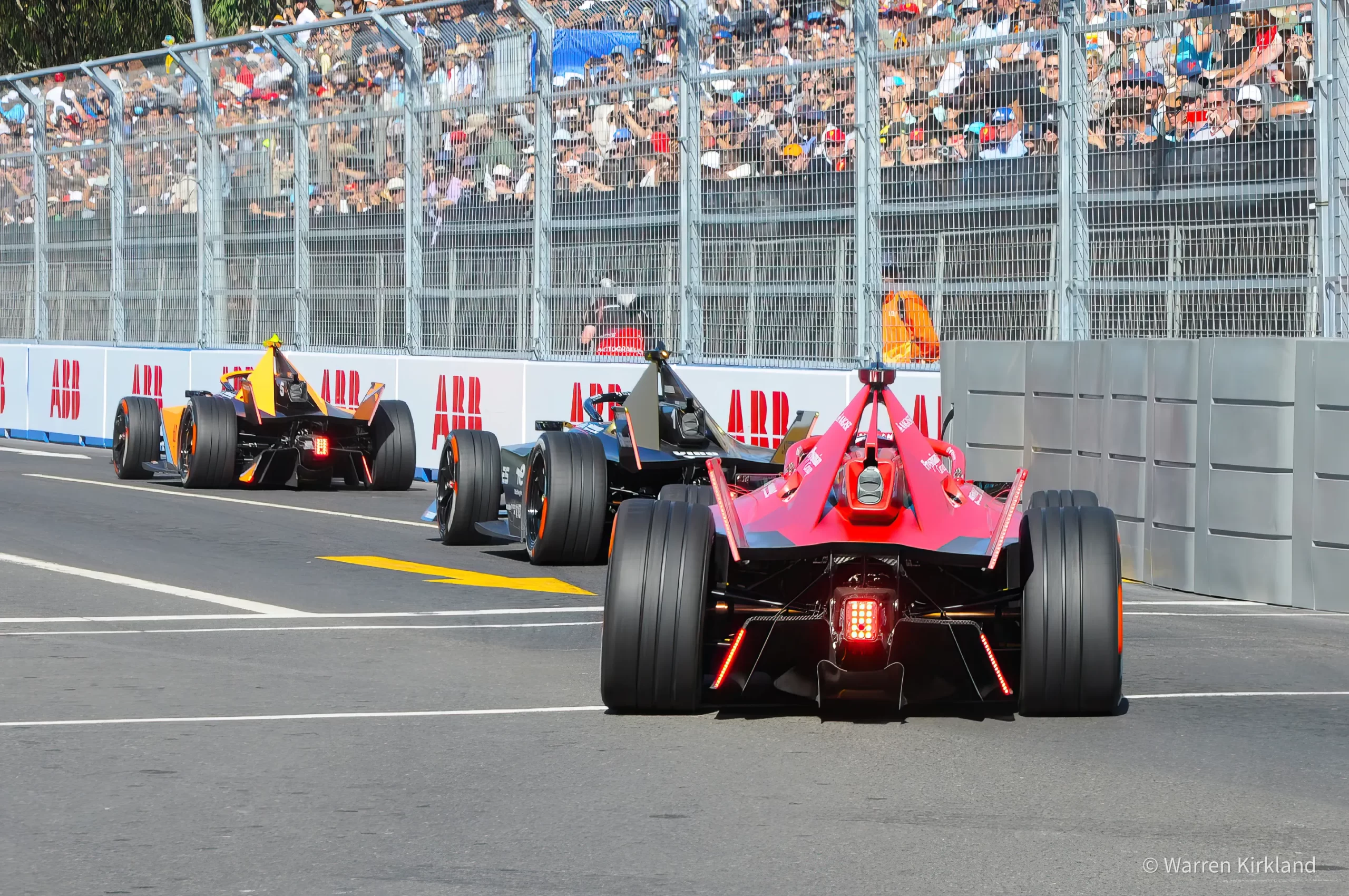 Formula E cars racing on a street circuit with a packed grandstand