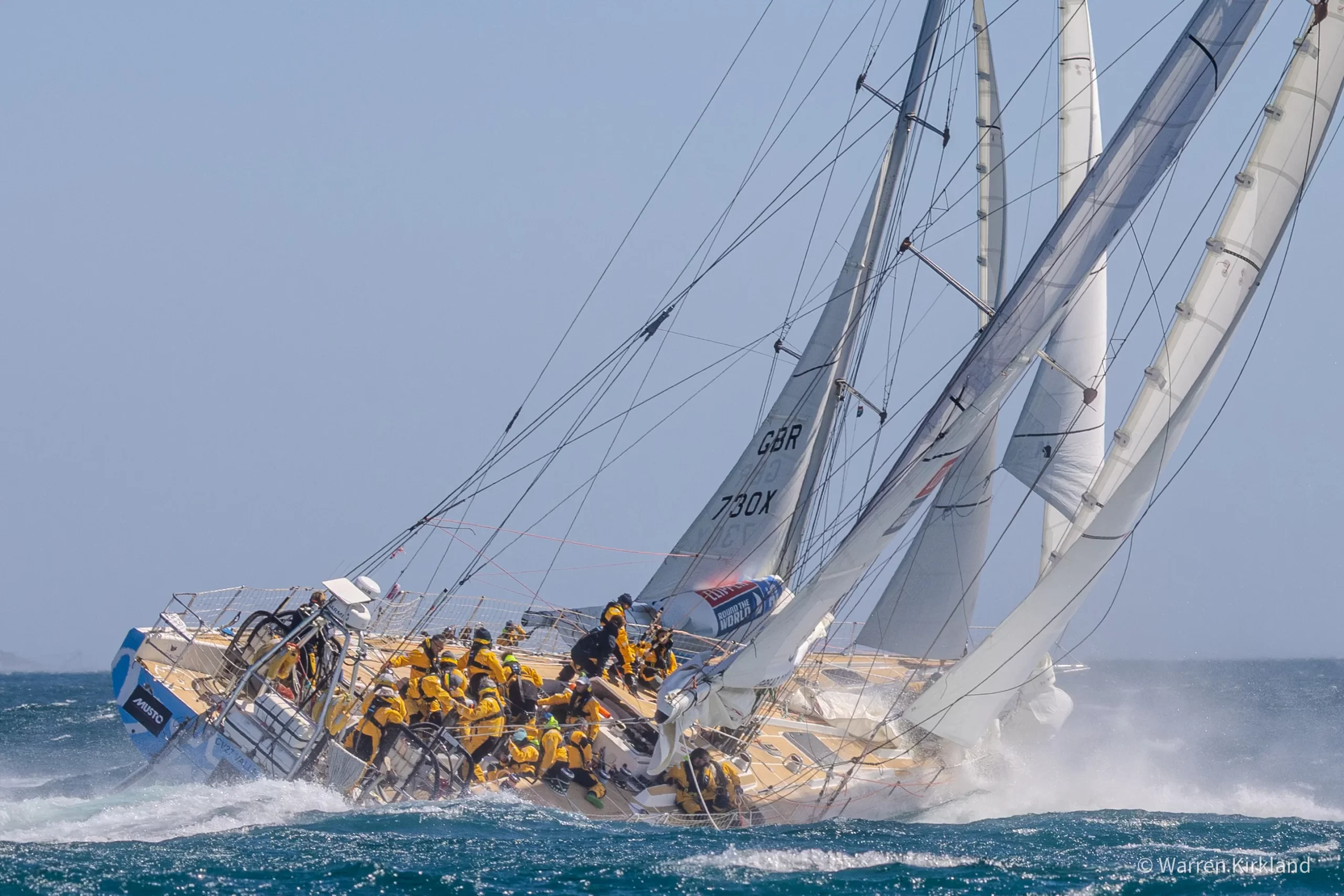 Clipper yacht heeling steeply with crew on the rail, spray flying