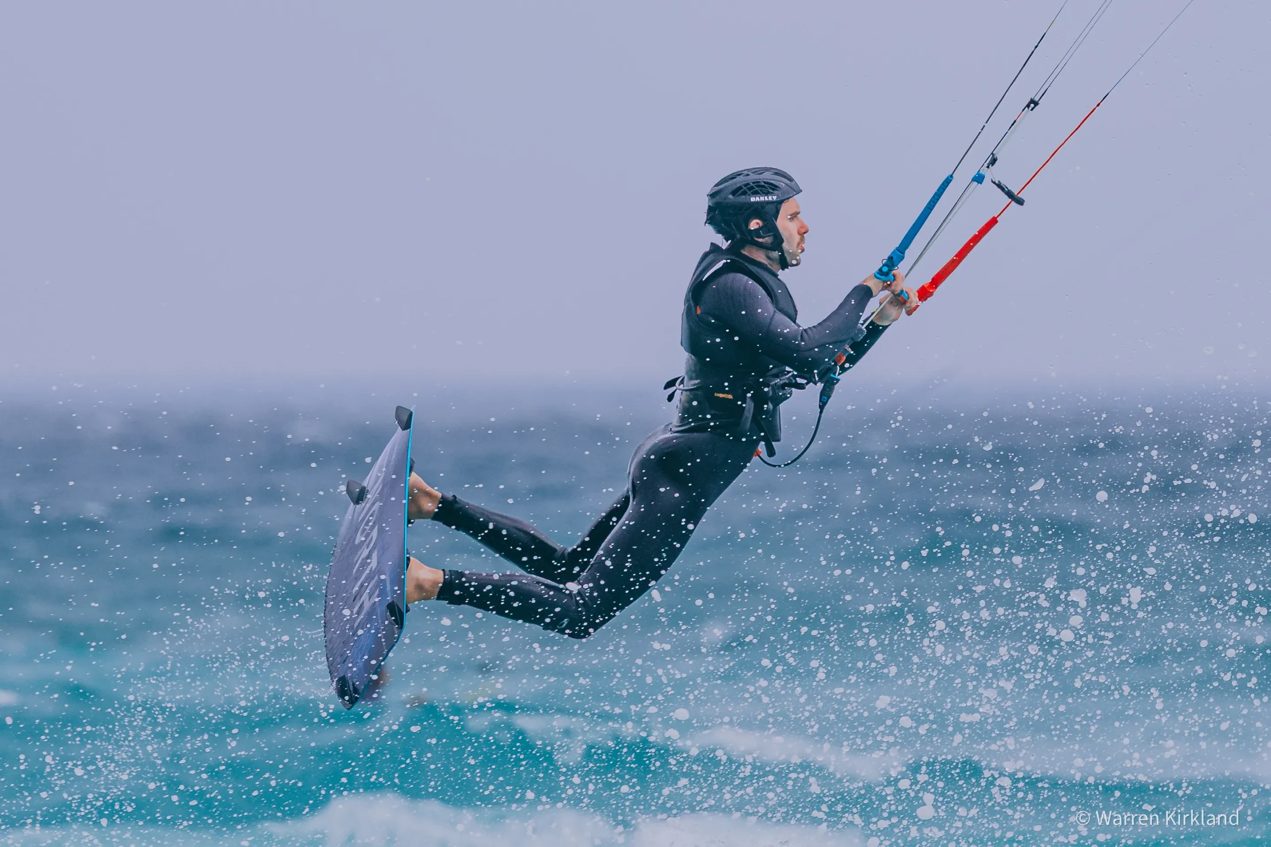 A kitesurfer mid-air above choppy turquoise ocean water.